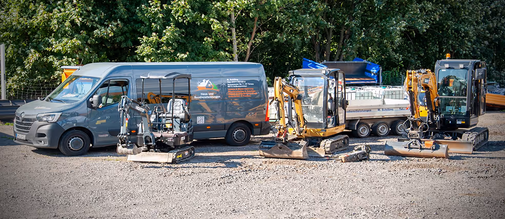 Ein grauer Transporter und drei verschiedene Minibagger stehen auf einem Kiesplatz vor Bäumen.